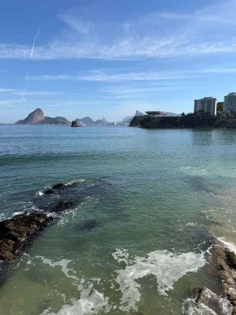 Mar sobre as pedras da orla de Niterói com o Pão de Açúcar no horizonte