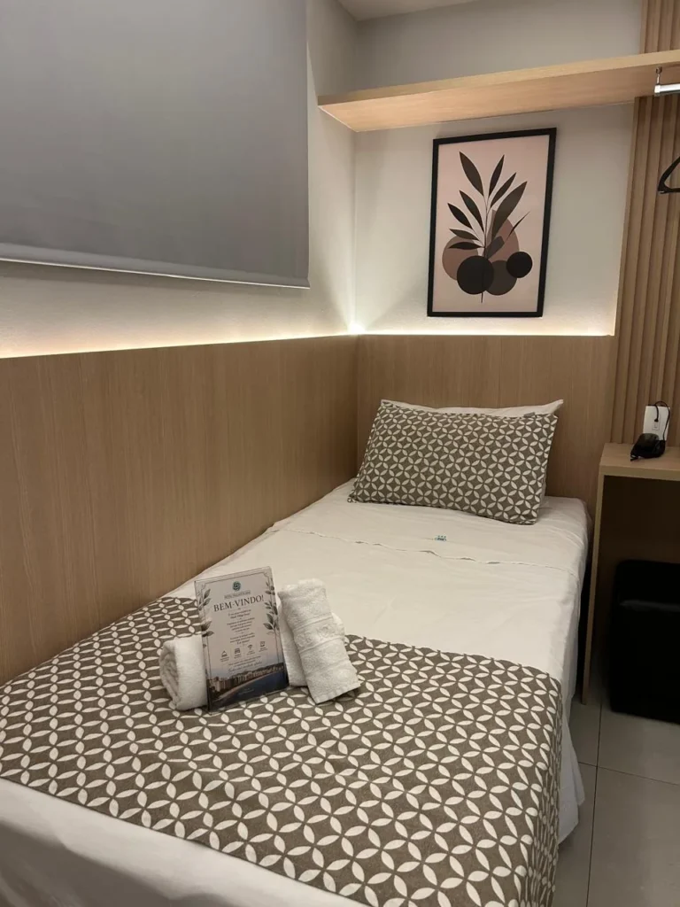 Cabeceira da minissuíte com quadro decorativo, cabideiro e iluminação indireta