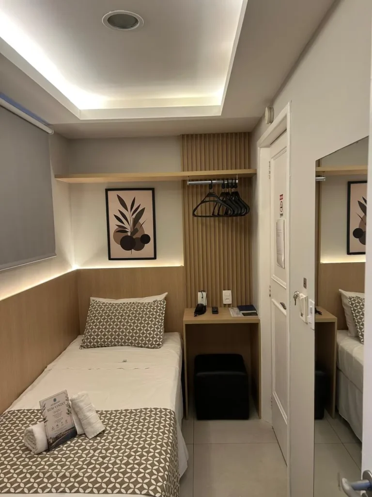 Minissuíte reformada vista da porta, com cama de solteiro, espelho e iluminação indireta