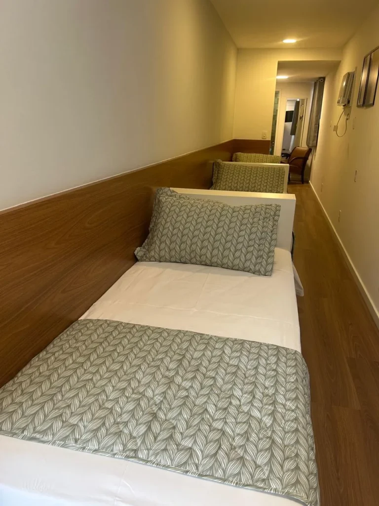 Cama de solteiro da Suíte Cápsula tripla com cabeceira de madeira e roupa de cama verde