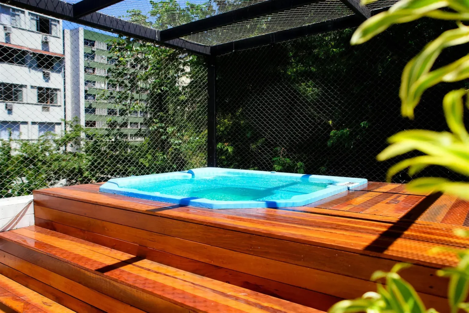 Hidromassagem azul com deck de madeira e plantas na cobertura do Hotel Village Icaraí, em dia de sol