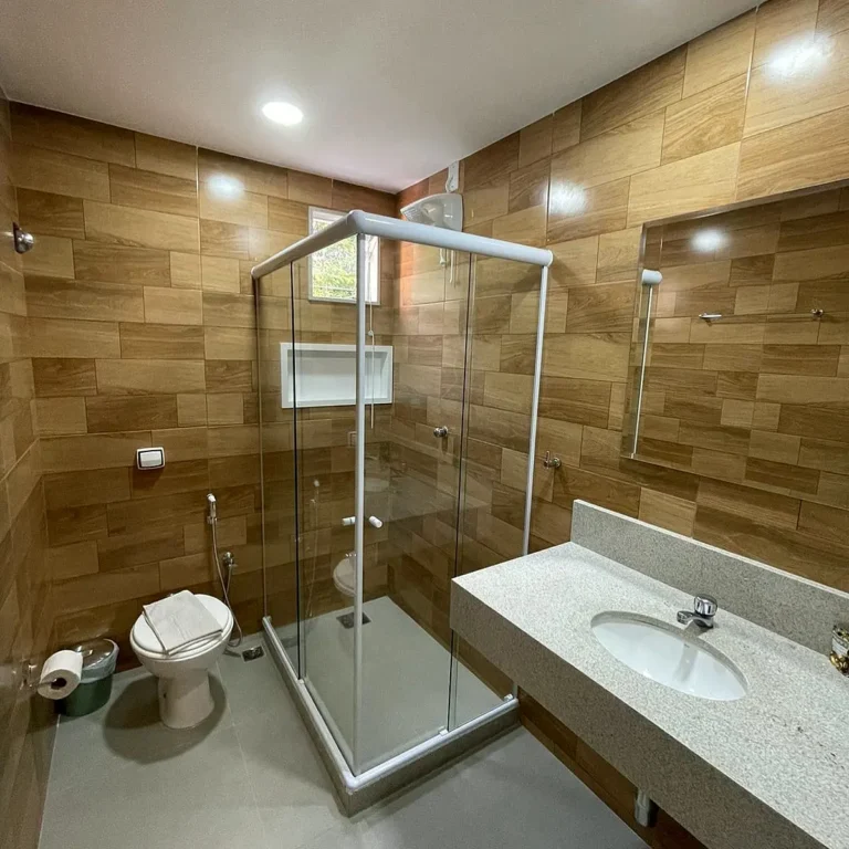 Banheiro com parede amadeirada, box de vidro e bancada de granito