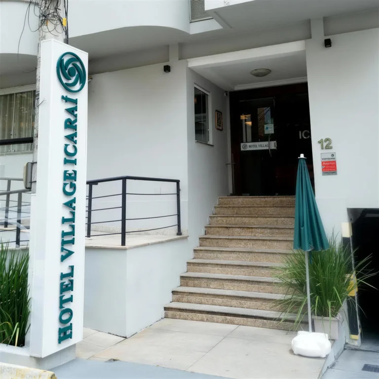 Entrada do Hotel Village Icaraí com escada e totem verde com o nome do hotel